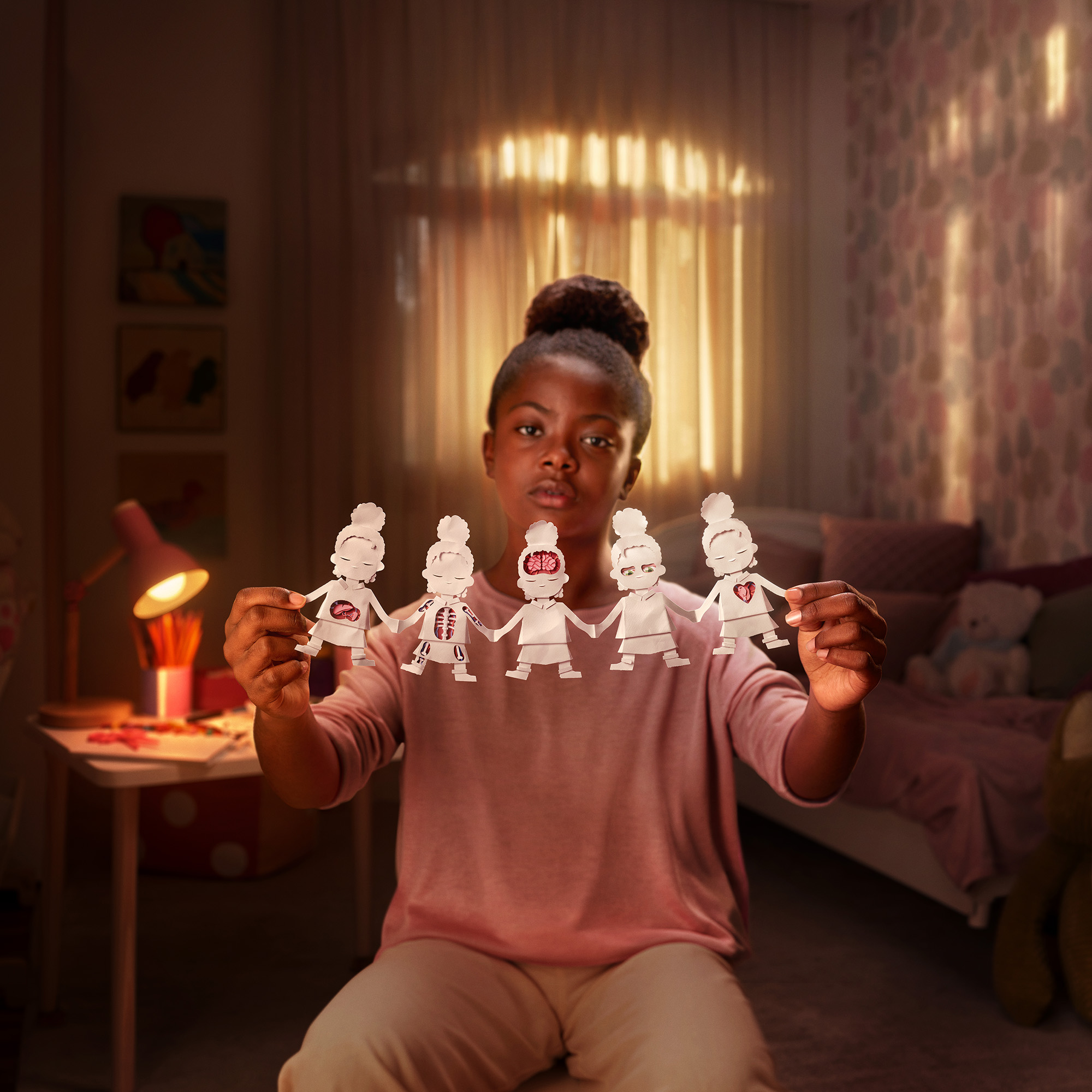 Girl holding the paper doll chain in a warmly lit bedroom